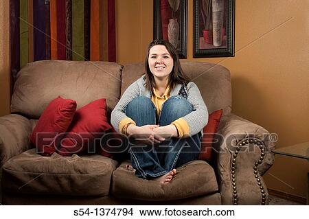 A young woman sitting on a couch indoors View Large Photo Image Picture - A young woman sitting on a couch indoors. Fotosearch