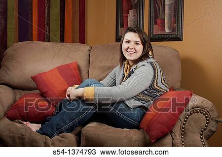 Stock Image - A young woman sitting on a couch indoors. Fotosearch