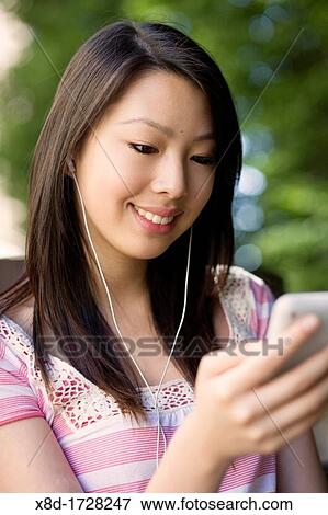 A young woman sitting on a park bench listening to her music player View Large Photo Image Stock Photo - A young woman sitting on a park bench listening to her music player. Fotosearch
