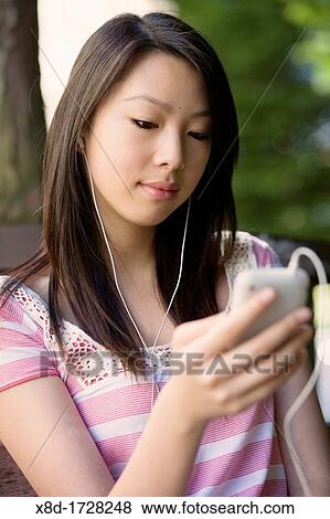 A young woman sitting on a park bench listening to her music player View Large Photo Image Stock Photo - A young woman sitting on a park bench listening to her music player. Fotosearch