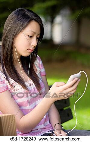 A young woman sitting on a park bench listening to her music player View Large Photo Image Stock Photo - A young woman sitting on a park bench listening to her music player. Fotosearch