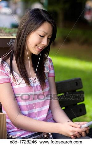 A young woman sitting on a park bench listening to her music player View Large Photo Image Stock Photograph - A young woman sitting on a park bench listening to her music player. Fotosearch