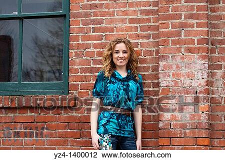 A young woman standing by a brick building View Large Photo Image Stock Image - A young woman standing by a brick building. Fotosearch