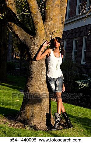 Stock Photography - A young woman stands against a tree in Cheney, Washington, USA.. Fotosearch