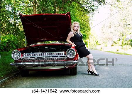 Stock Image - A young woman with a red 1964 Dodge Dart with the hood up.. Fotosearch
