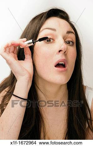 A young woman with brown hair and eyes applying her makeup - putting on mascara View Large Photo Image Picture - A young woman with brown hair and eyes applying her makeup - putting on mascara. Fotosearch