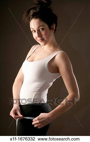 Stock Image - A young woman with brown hair and eyes measuring her body - checking the size of her bottom bum arse. Fotosearch