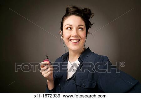 Stock Photo - A young woman with brown hair and eyes listening top music on her small iPod Nano MP3 player. Fotosearch