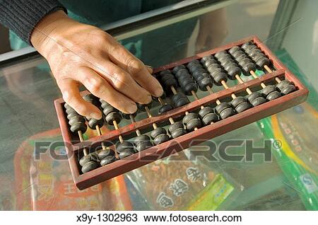 Stock Image - Abacus counting machine calculator Woman hand using abacus adding subtracting sum on shop counter in Chinese shop, China. Fotosearch