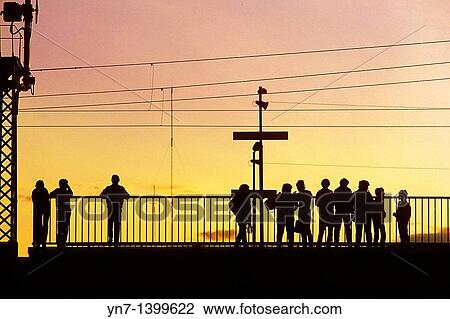 Stock Image - Abstract pattern of silhouettes of travellers at a suburban train station in the glow of early evening. Fotosearch