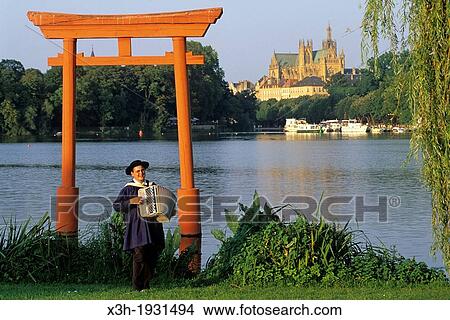 Picture - accordionist under the Torii on Saint-Symphorien island with the cathedrale in background, Metz, Moselle department, Lorraine region, France, Europe. Fotosearch