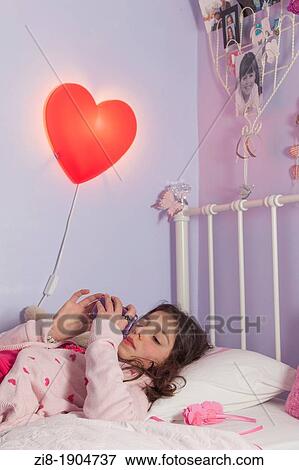 Adolecent girl playing games on her mobile phone in bed View Large Photo Image Stock Photo - Adolecent girl playing games on her mobile phone in bed. Fotosearch
