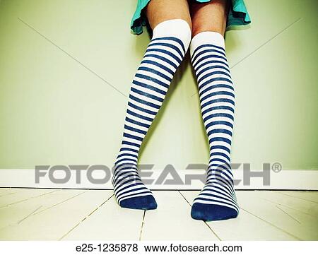 Stock Photo - Adult female wearing stripey socks stands against a wall on a wooden floor painted white. Fotosearch
