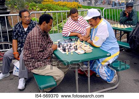 Stock Image - Adult men looks over game pieces on a chess board as they play chess in a downtown detroit michigan park. Fotosearch