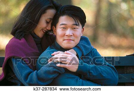 Affectionate asian couple sitting on park bench View Large Photo Image Picture - Affectionate asian couple sitting on park bench. Fotosearch
