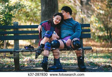 Affectionate asian couple sitting on park bench after rollerblading, wearing knee pads and roller blades View Large Photo Image Stock Image - Affectionate asian couple sitting on park bench after rollerblading, wearing knee pads and roller blades. Fotosearch