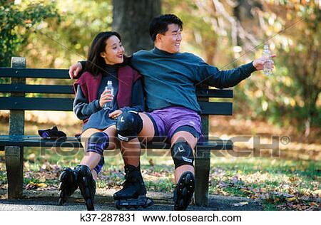 Affectionate asian couple sitting on park bench after rollerblading, wearing knee pads and roller blades View Large Photo Image Stock Image - Affectionate asian couple sitting on park bench after rollerblading, wearing knee pads and roller blades. Fotosearch