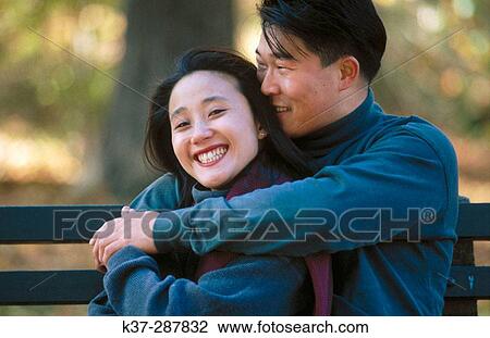 Affectionate asian couple sitting on park bench View Large Photo Image Stock Image - Affectionate asian couple sitting on park bench. Fotosearch