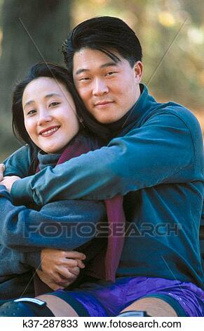 Stock Image - Affectionate asian couple sitting on park bench. Fotosearch
