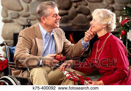 Stock Image - Affectionate senior couple exchanging Christmas presents. Fotosearch