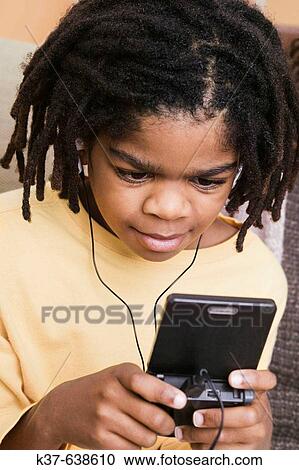 Stock Image - African-American boy playing on gameboy at home.. Fotosearch