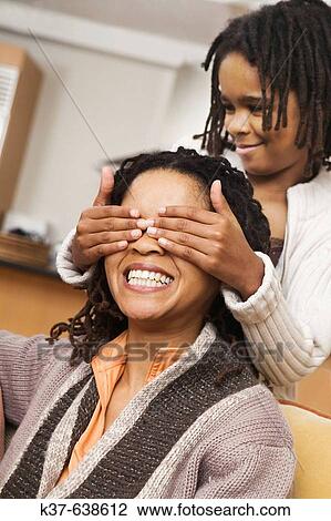 African American family at home, parents on sofa & daughter covering mother's eyes with hands from behind. Guess who? View Large Photo Image Stock Image - African American family at home, parents on sofa & daughter covering mother's eyes with hands from behind. Guess who?. Fotosearch