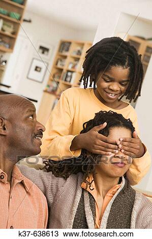 African American family at home, parents on sofa, son covering mother's eyes with hands from behind. Guess who? View Large Photo Image Stock Image - African American family at home, parents on sofa, son covering mother's eyes with hands from behind. Guess who?. Fotosearch