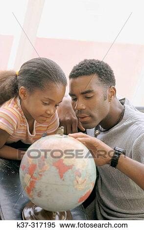 Stock Photography - African-American father and daughter looking at globe. Fotosearch
