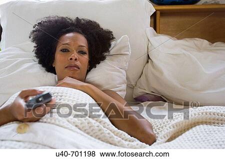 Stock Photo - African American woman watching TV in bed. Fotosearch