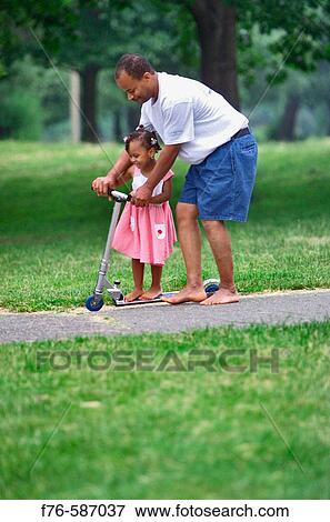 Afro American father helping his daughter ride a scooter. View Large Photo Image Stock Photo - Afro American father helping his daughter ride a scooter.. Fotosearch
