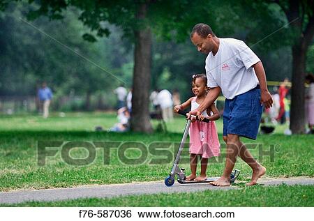 Afro American father helping his daughter ride a scooter. View Large Photo Image Stock Photograph - Afro American father helping his daughter ride a scooter.. Fotosearch