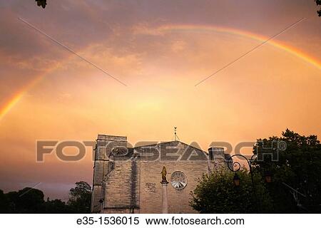 Stock Photography - After a rainstorm a rainbow appears over the 13th century Church of St. Saturnin on the outskirts of Pezenas, France. Fotosearch