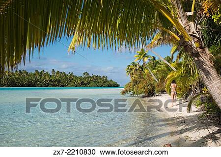 Aitutaki. Cook Island. Polynesia. South Pacific Ocean. A tourist walks along the edge of the palm-fringed beach in One Foot Island. View Large Photo Image Stock Image - Aitutaki. Cook Island. Polynesia. South Pacific Ocean. A tourist walks along the edge of the palm-fringed beach in One Foot Island.. Fotosearch
