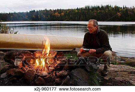 Stock Photo - Algonquin Provincial Park, Ontario - John West, 61, sits by the campfire while camped on Rain Lake during a canoe camping trip MR. Fotosearch