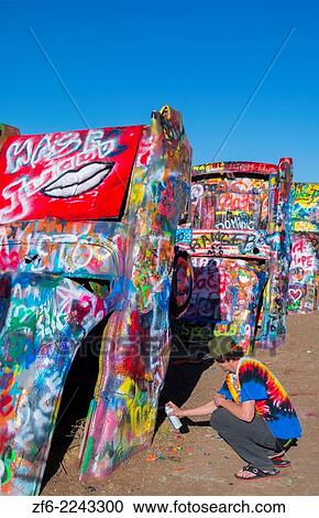 Stock Image - Amarillo Texas famous Cadillac Ranch teen spraying paint off of Route 66 old Cadillacs buiried in ground on Rt 66 9.. Fotosearch