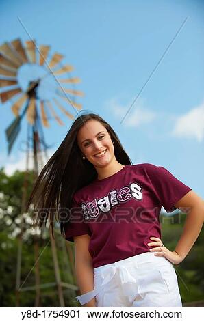 Stock Image - American female highschool senior in front of ranch wind turbine. Fotosearch