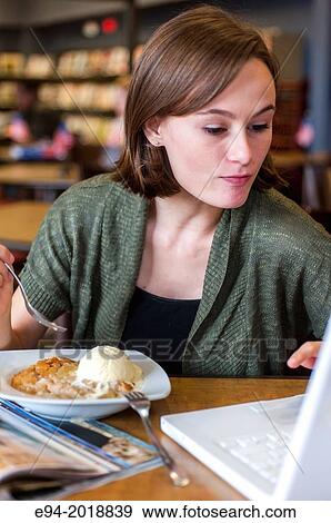 An 18 year old girl in a library reading from a computer screen with a dessert on the table. View Large Photo Image Stock Photo - An 18 year old girl in a library reading from a computer screen with a dessert on the table.. Fotosearch