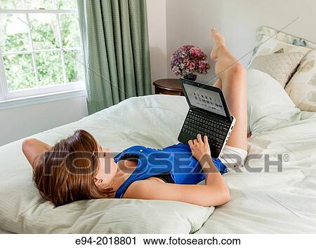 An 18 year old girl lying on her bed looking at a computer screen. View Large Photo Image Stock Image - An 18 year old girl lying on her bed looking at a computer screen.. Fotosearch