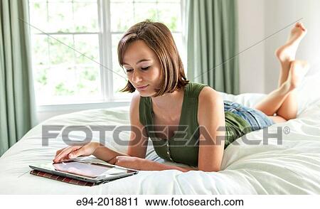 An 18 year old girl lying on her bed reading from a pad computer,. View Large Photo Image Stock Image - An 18 year old girl lying on her bed reading from a pad computer,.. Fotosearch
