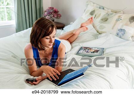An 18 year old girl lying on her bed with a computer, text book and cell phone. View Large Photo Image Stock Photo - An 18 year old girl lying on her bed with a computer, text book and cell phone.. Fotosearch
