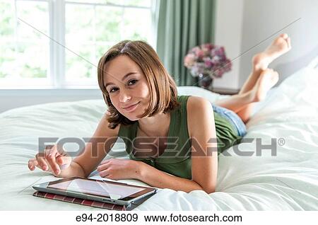 An 18 year old girl lying on her bed reading from a pad computer,. View Large Photo Image Stock Photo - An 18 year old girl lying on her bed reading from a pad computer,.. Fotosearch