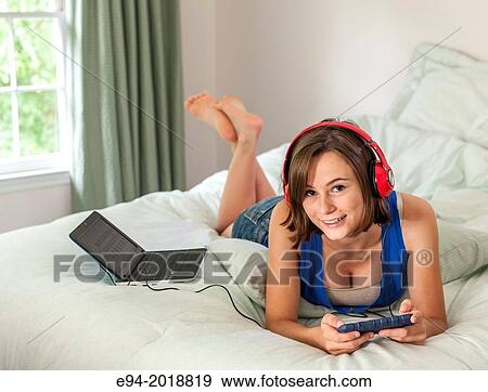 An 18 year old girl lying on her bed texting and weaing head phones. View Large Photo Image Stock Photo - An 18 year old girl lying on her bed texting and weaing head phones.. Fotosearch