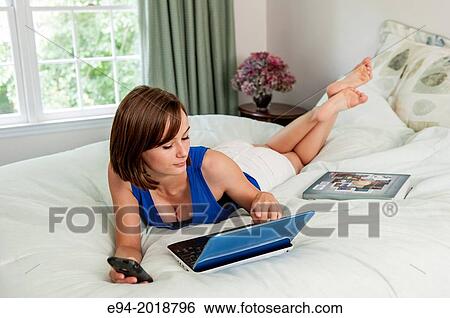 Stock Photograph - An 18 year old girl lying on her bed with a computer, text book and cell phone.. Fotosearch