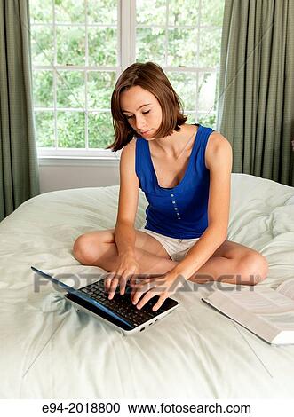 An 18 year old girl sitting on her bed with a computer, text book and cell phone. View Large Photo Image Stock Image - An 18 year old girl sitting on her bed with a computer, text book and cell phone.. Fotosearch
