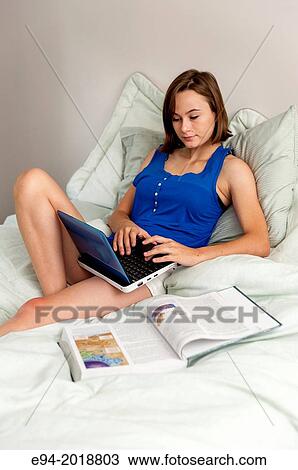 Stock Image - An 18 year old girl sitting on her bed with a computer, text book and cell phone.. Fotosearch