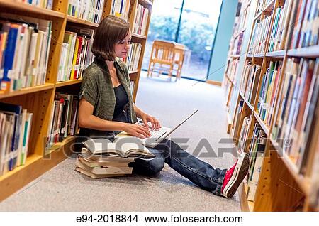 An 18 year old girl sitting on the floor in a library with a laptop computer and books stacked next to her. View Large Photo Image Picture - An 18 year old girl sitting on the floor in a library with a laptop computer and books stacked next to her.. Fotosearch