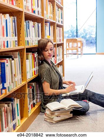 An 18 year old girl sitting on the floor in a library with a laptop computer and books stacked next to her. View Large Photo Image Stock Image - An 18 year old girl sitting on the floor in a library with a laptop computer and books stacked next to her.. Fotosearch
