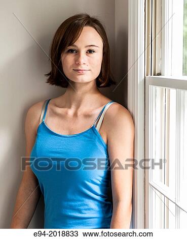 Stock Image - An 18 year old girl standing by a window in a house looking at the camera.. Fotosearch