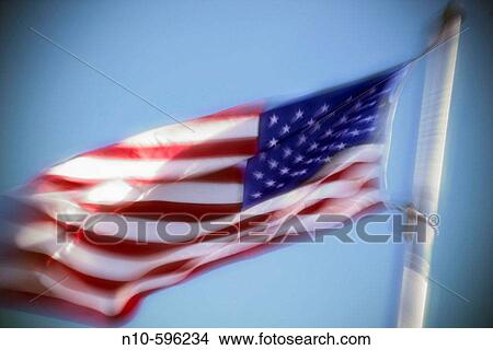 An American flag billowing in the wind against a blue sky. View Large Photo Image Picture - An American flag billowing in the wind against a blue sky.. Fotosearch