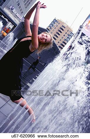 Stock Photograph - An aspiring actress gleefully runs through a series of fountains situated right in the midst of downtown Toronto Canada. Shot in October, 2006. Fotosearch